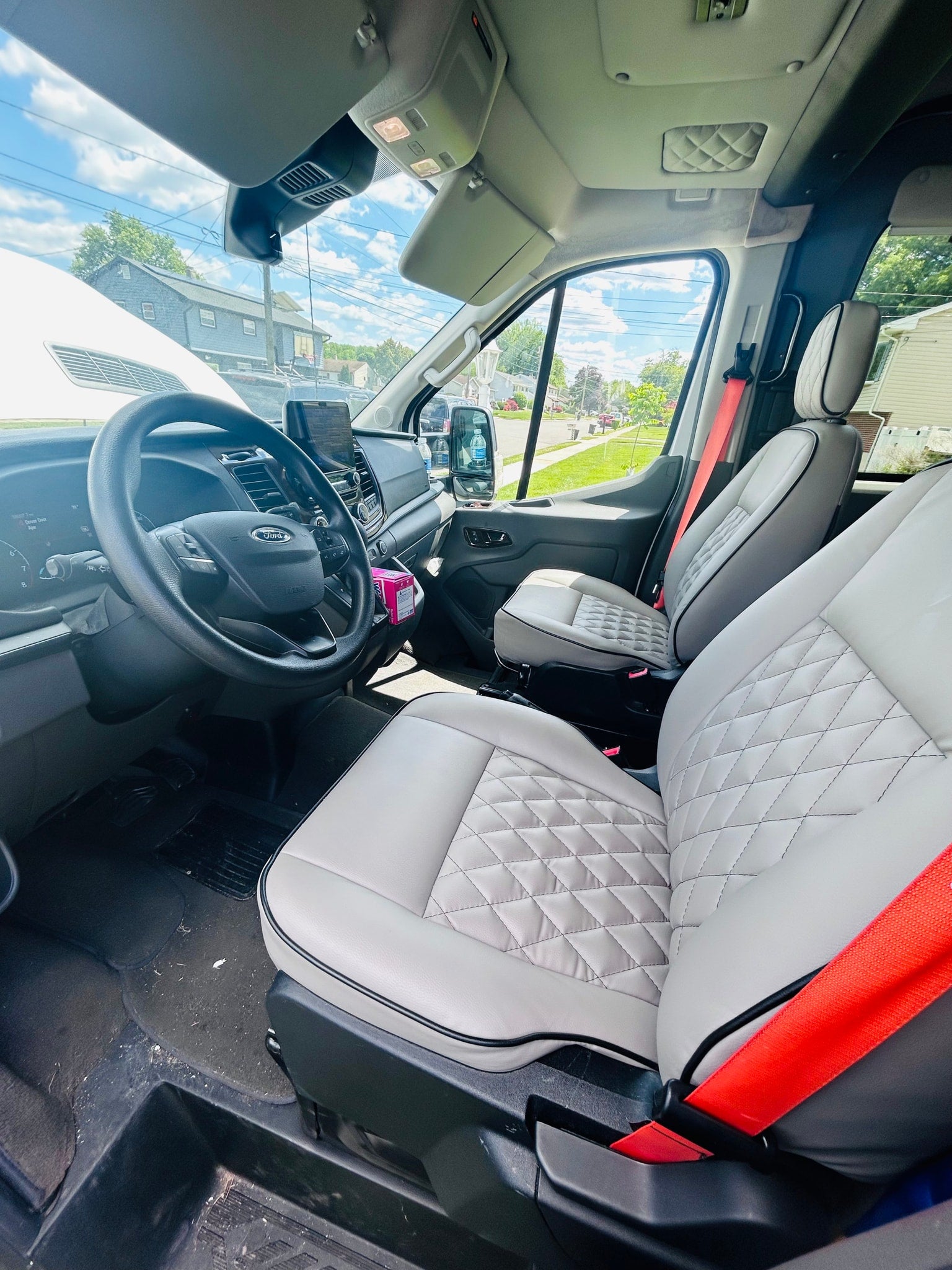 Spacious Ford van interior for rv rental: light grey quilted seats, dashboard view, and bright red seatbelts detail the front cabin.