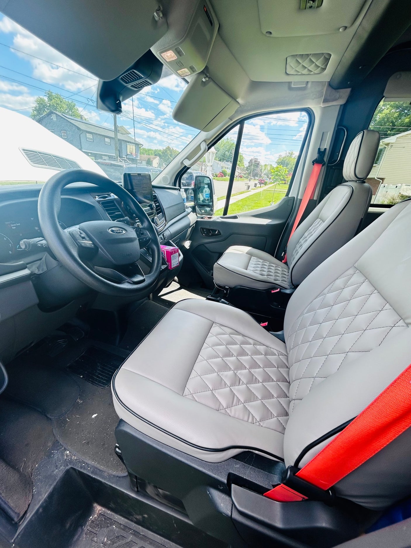 Spacious Ford van interior for rv rental: light grey quilted seats, dashboard view, and bright red seatbelts detail the front cabin.