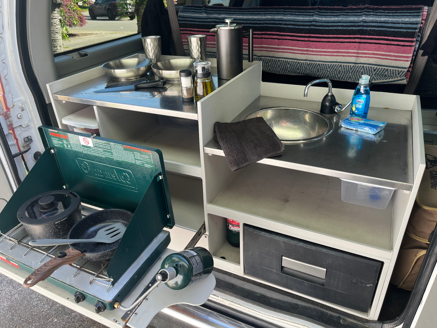Compact RV rental kitchen setup with propane stove, sink, and cooking essentials. Perfect for camping meals.