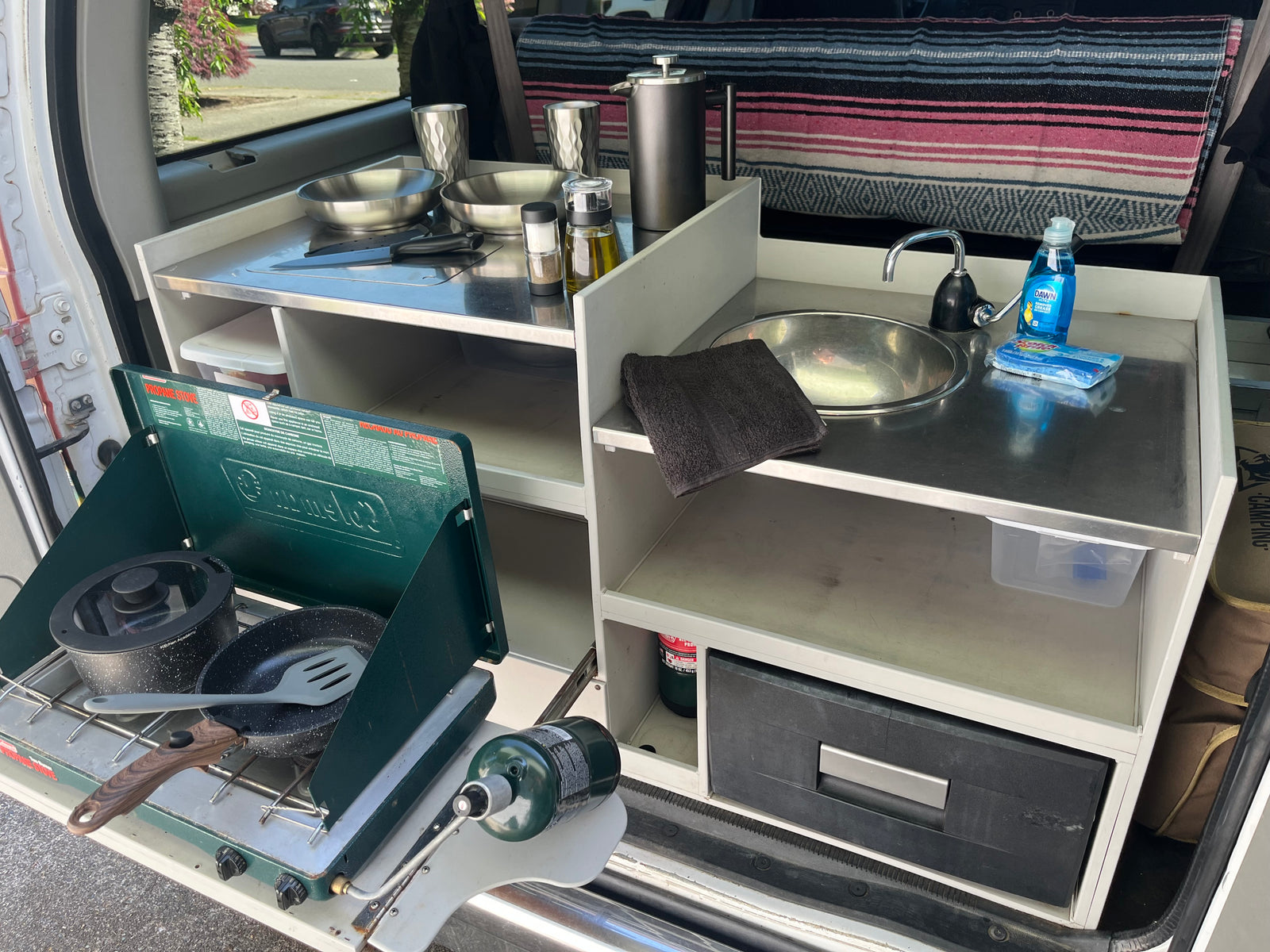 Compact RV rental kitchen setup with propane stove, sink, and cooking essentials. Perfect for camping meals.