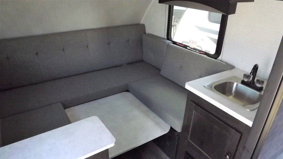 neatly lined up on a sunny gravel lot.|This RV rental interior showcases an L-shaped grey dinette