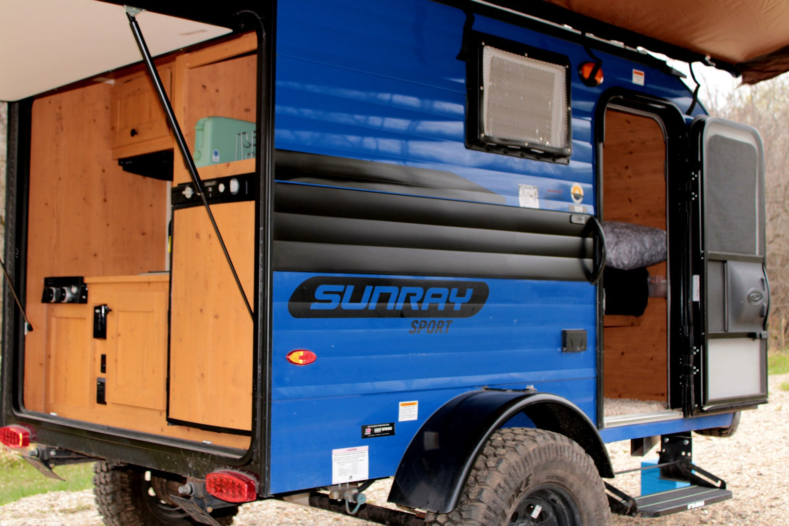 Blue Sunray Sport teardrop camper RV rental with an open rear kitchen and side door, ready for outdoor adventures.