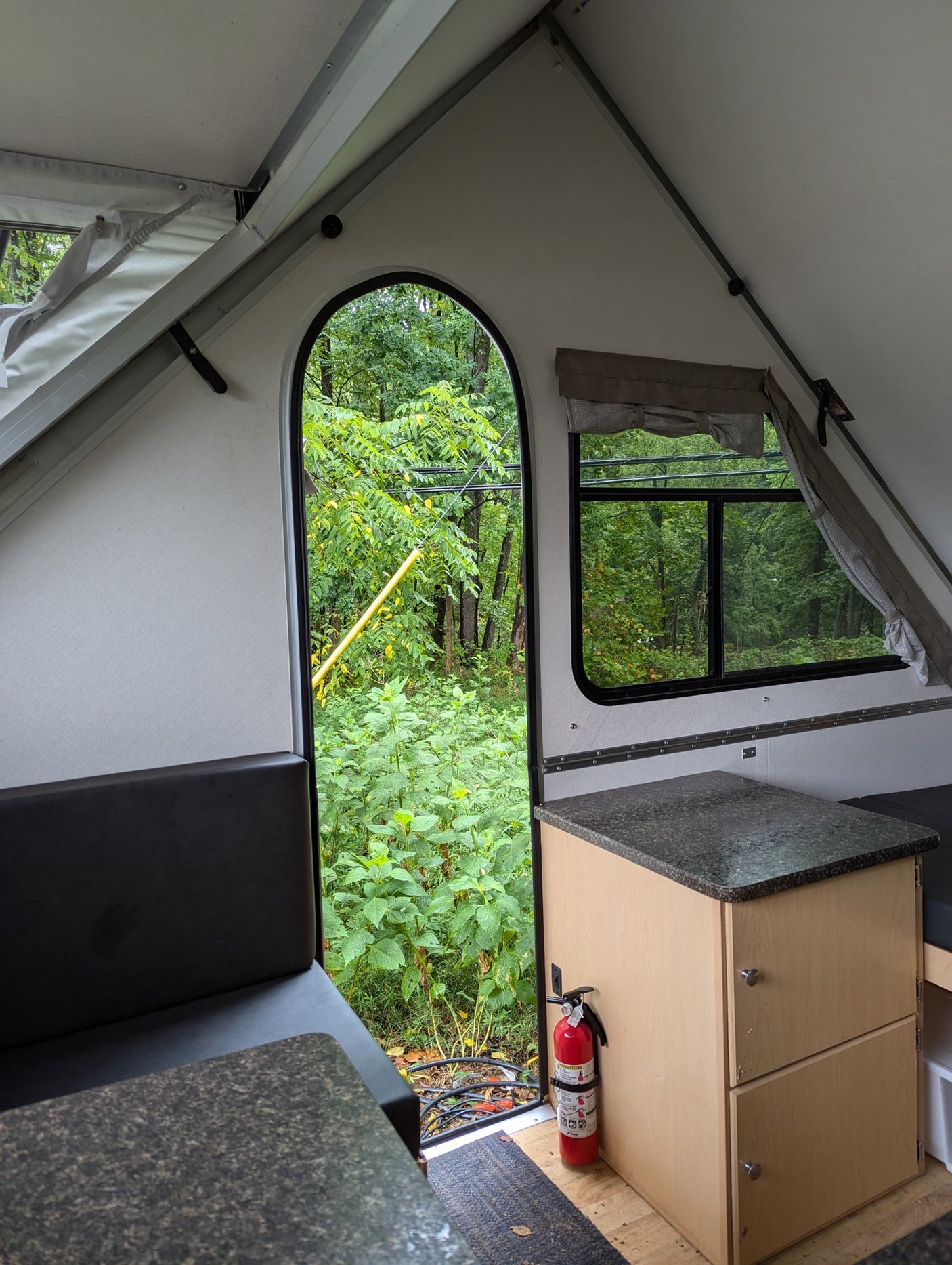 Cozy A-frame rv rental interior showcasing a forest view, compact kitchen, and fire safety.