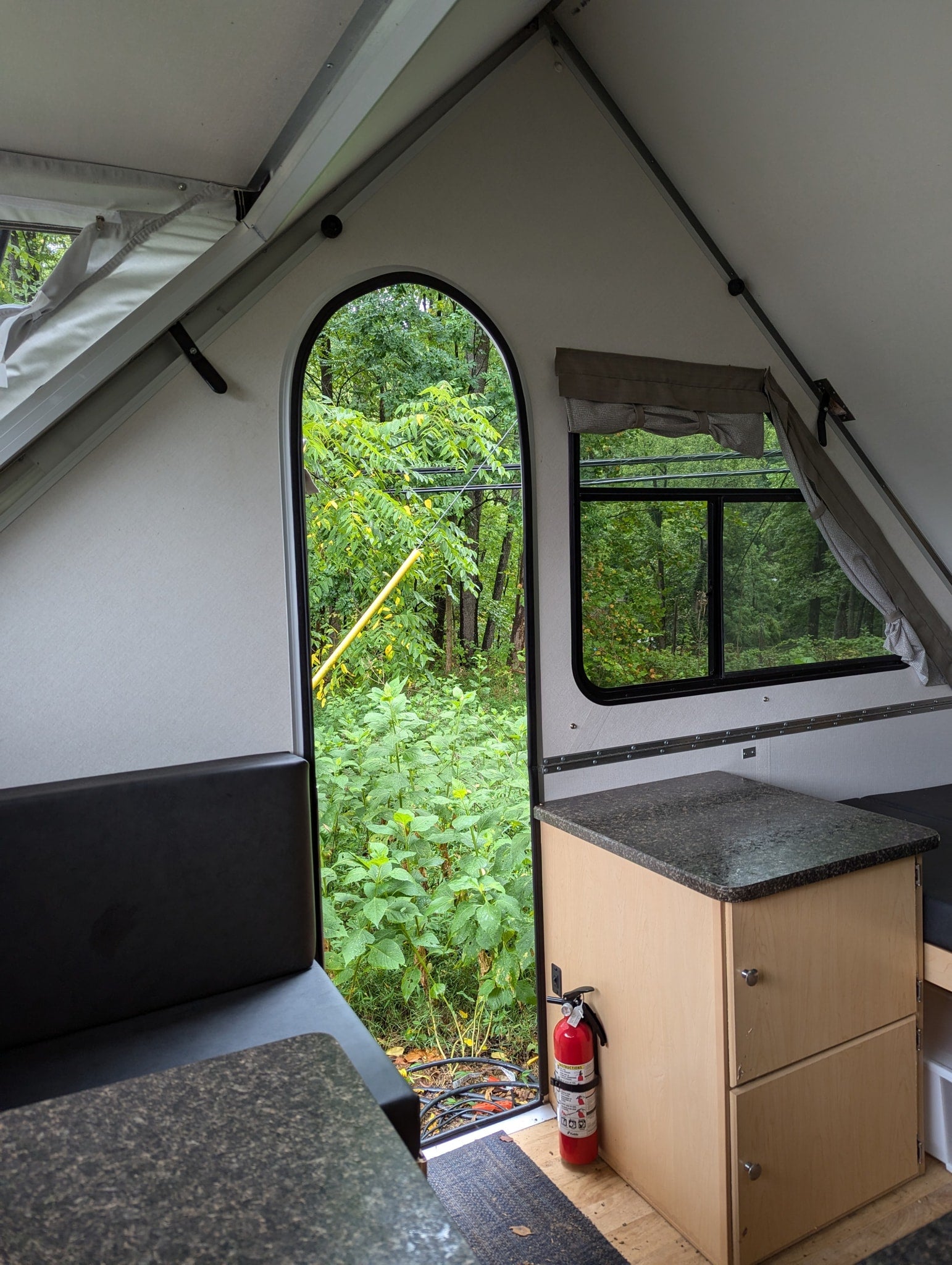 Cozy A-frame rv rental interior showcasing a forest view, compact kitchen, and fire safety.