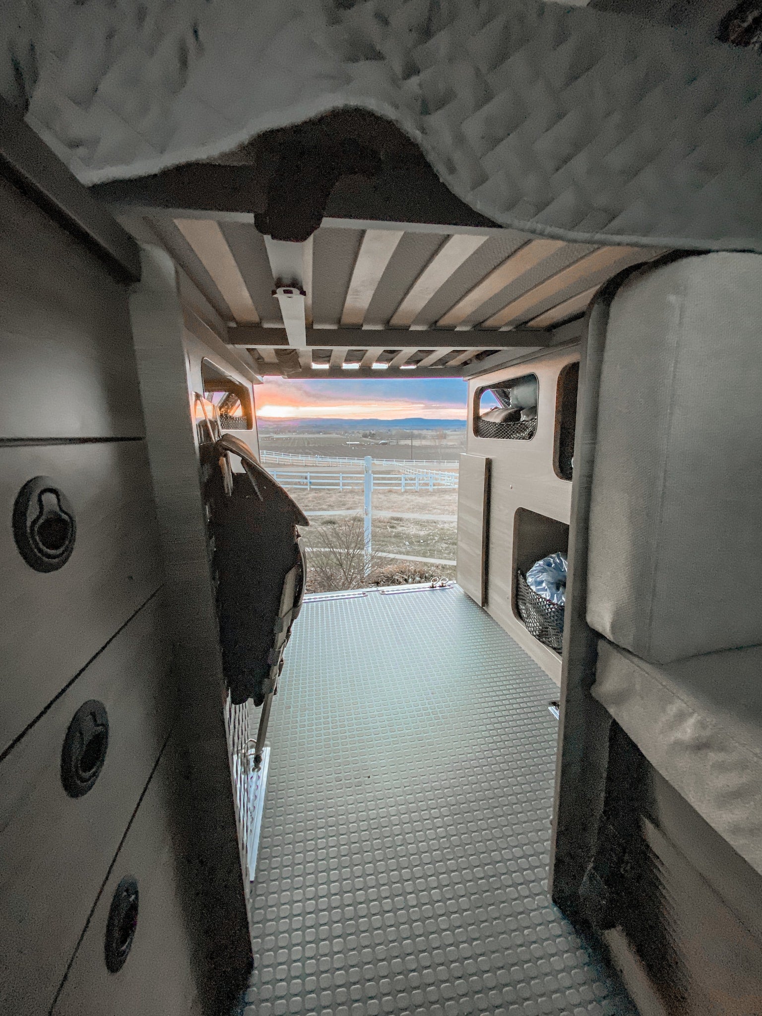 RV rental interior at sunset. View from the back of a spacious camper van with textured flooring & comfortable sleeping areas.