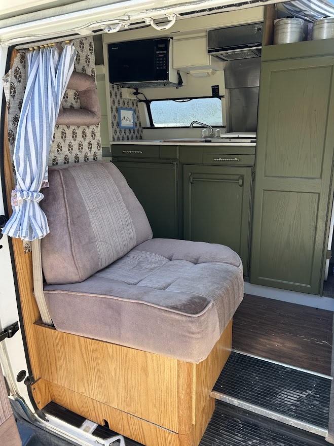 Cozy RV rental interior with olive green kitchenette (microwave, sink) and plush seating. Perfect camper van setup!