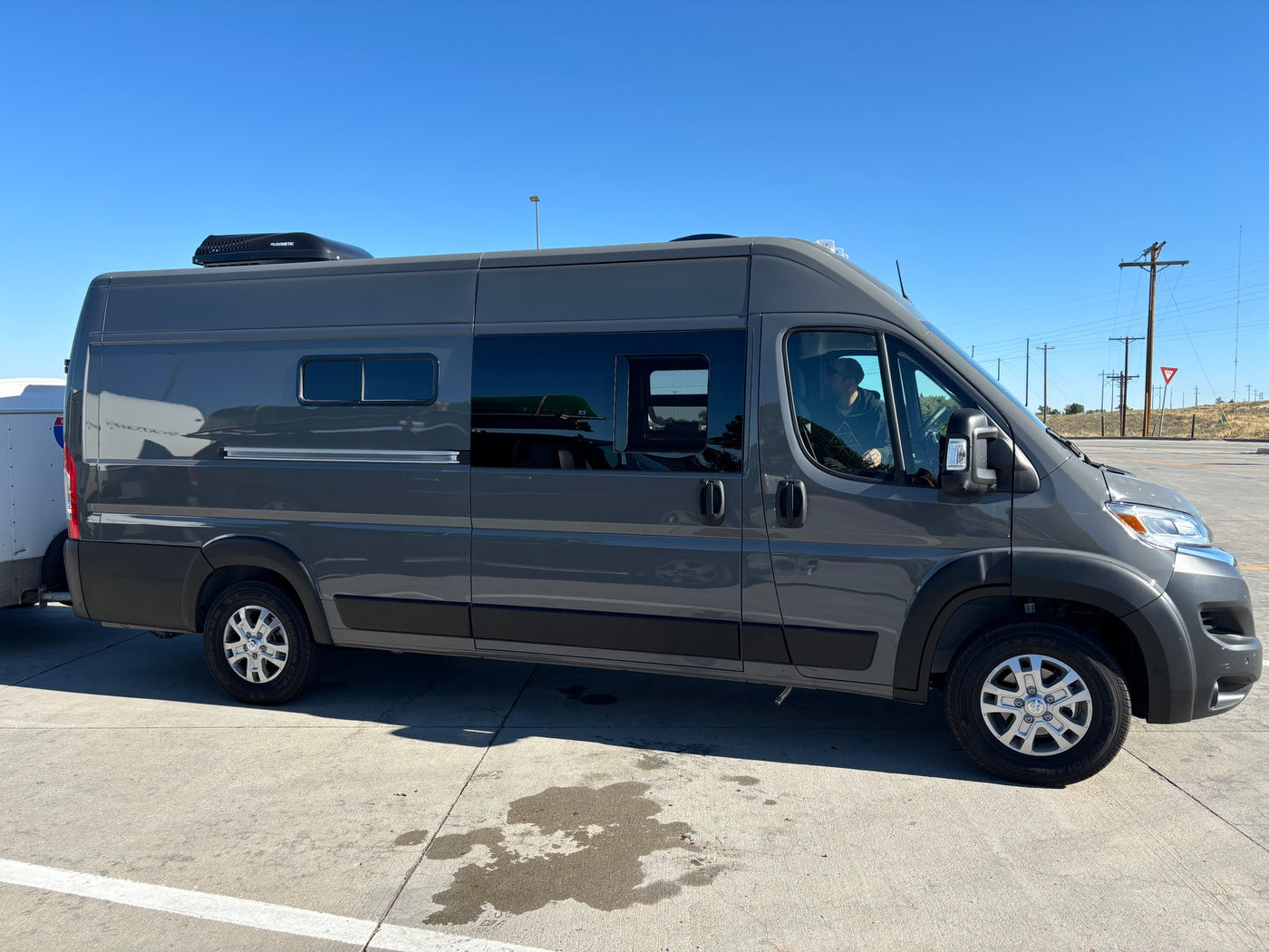 This grey camper van, an RV rental, is hitched to a trailer for a sunny road trip adventure under a clear blue sky. — photo 17