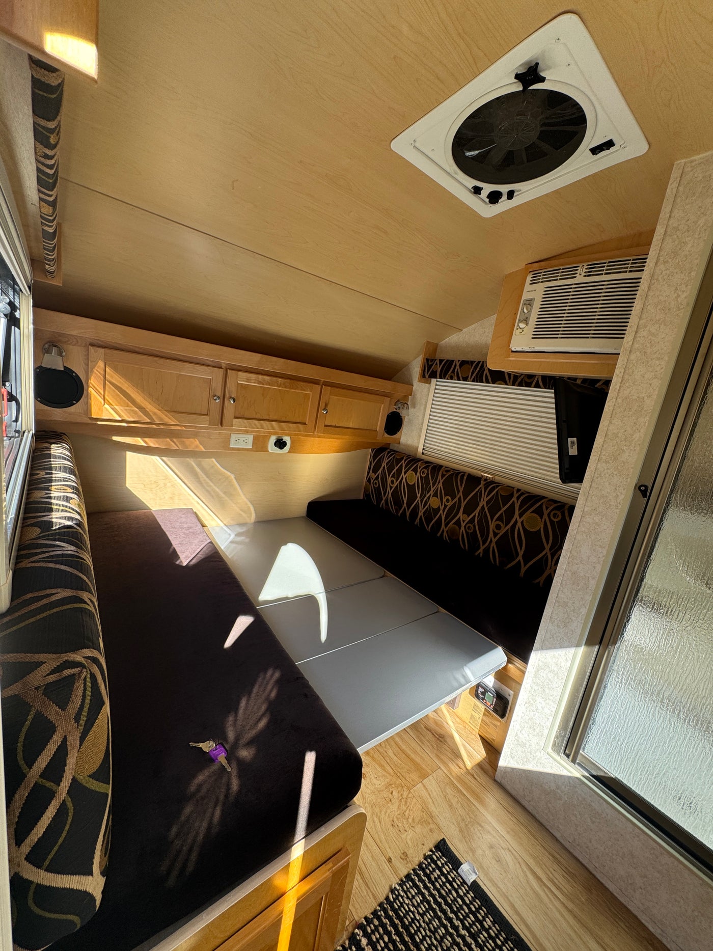 Cozy RV rental interior: convertible dining/bed area, wooden cabinets, AC, and ceiling fan visible in a sunlit camper. — photo 14