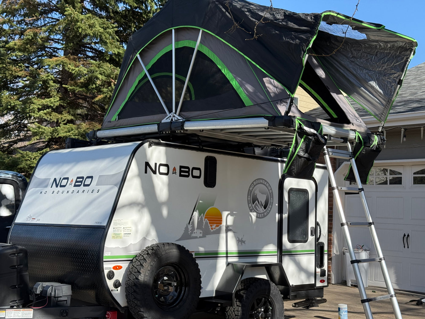 NO BO RV rental: A white No Boundaries camper with an open rooftop tent & ladder for your next outdoor adventure.
