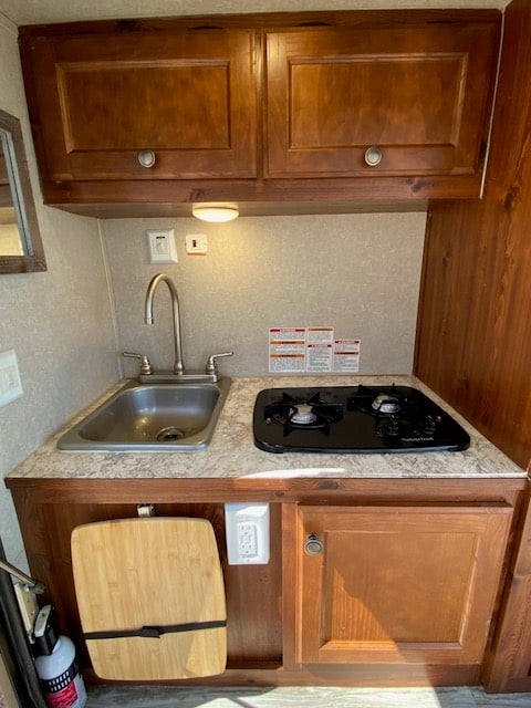 Inside an RV rental: a practical kitchen setup with a sink, two-burner stove, and ample storage in wood cabinets.