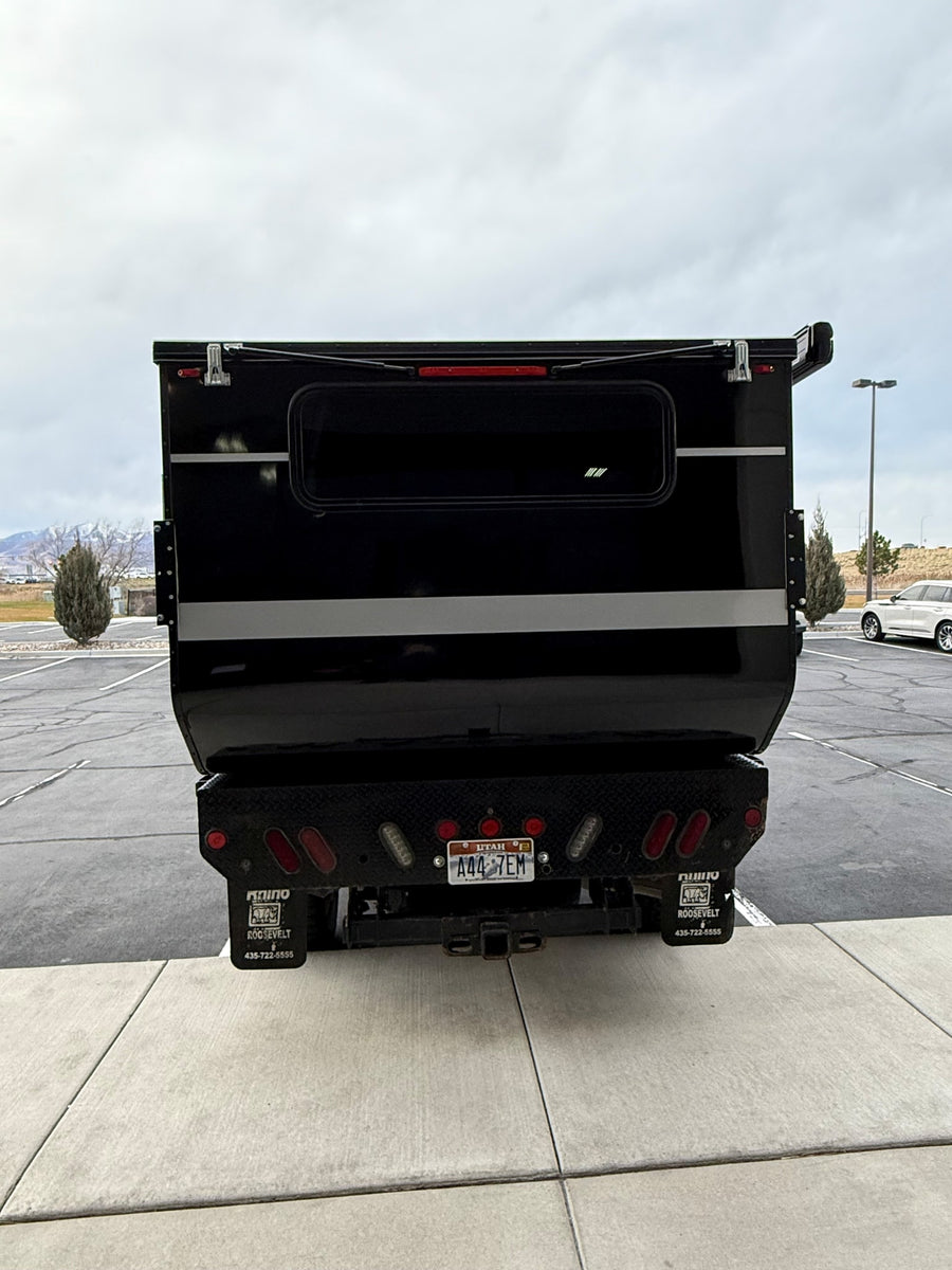 Rear of black pop-up truck camper RV rental, Utah plate A44 7EM, with Rhino mud flaps. Parked in lot.