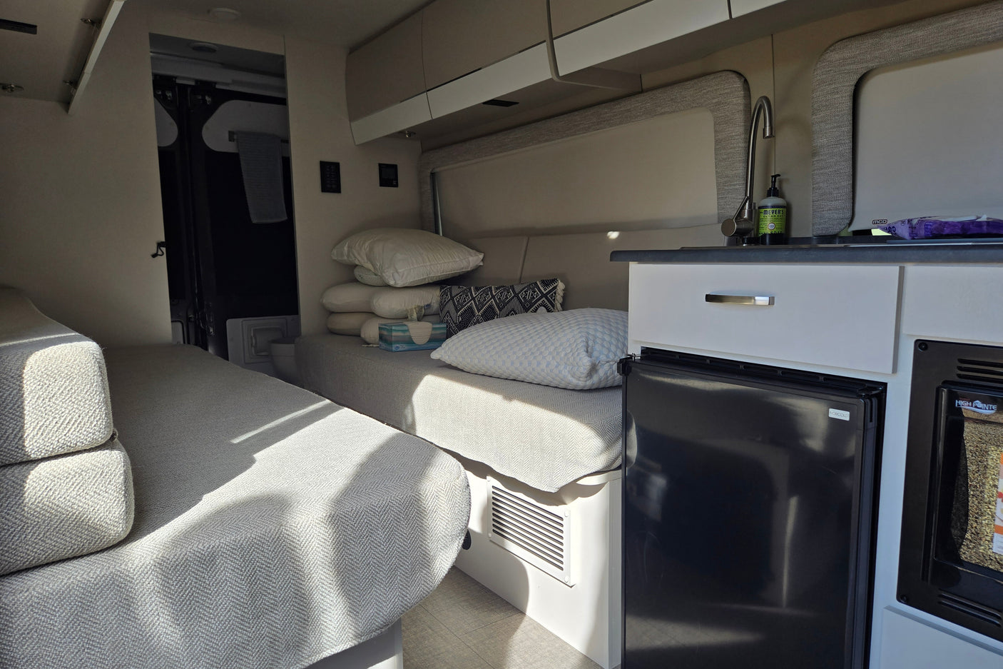 Inside a modern rv rental: twin beds, compact kitchen with sink & fridge. A cozy, functional living space.