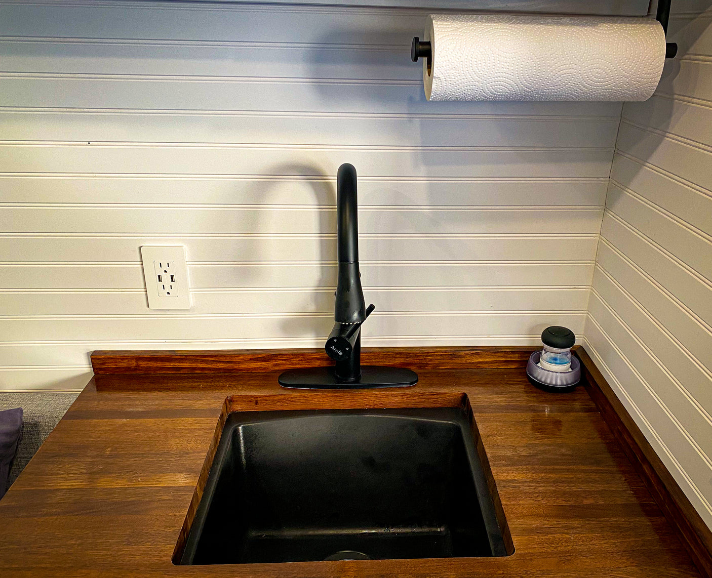 RV rental kitchen: modern black sink, faucet, wood counter, white walls, and a convenient outlet with USB ports.