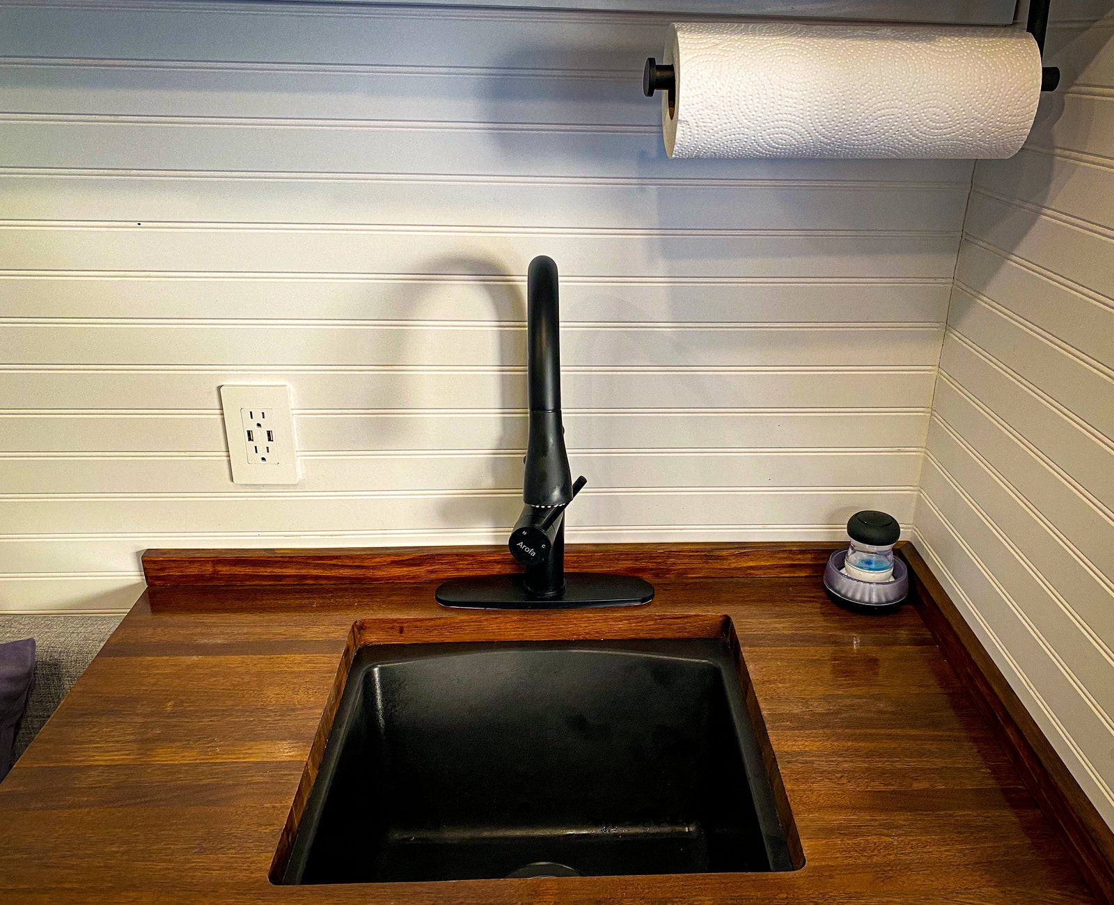RV rental kitchen: modern black sink, faucet, wood counter, white walls, and a convenient outlet with USB ports.