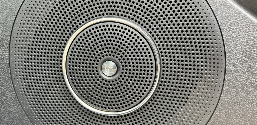 RV rental: High-fidelity B&O audio speaker grille, showing perforated pattern and chrome ring.