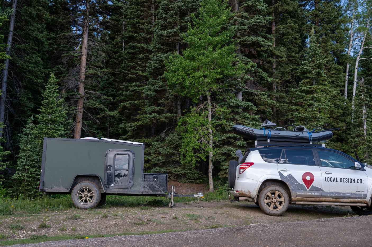 Adventure-ready: an RV rental trailer and SUV with raft, parked by a dense forest. Ideal for exploring nature.