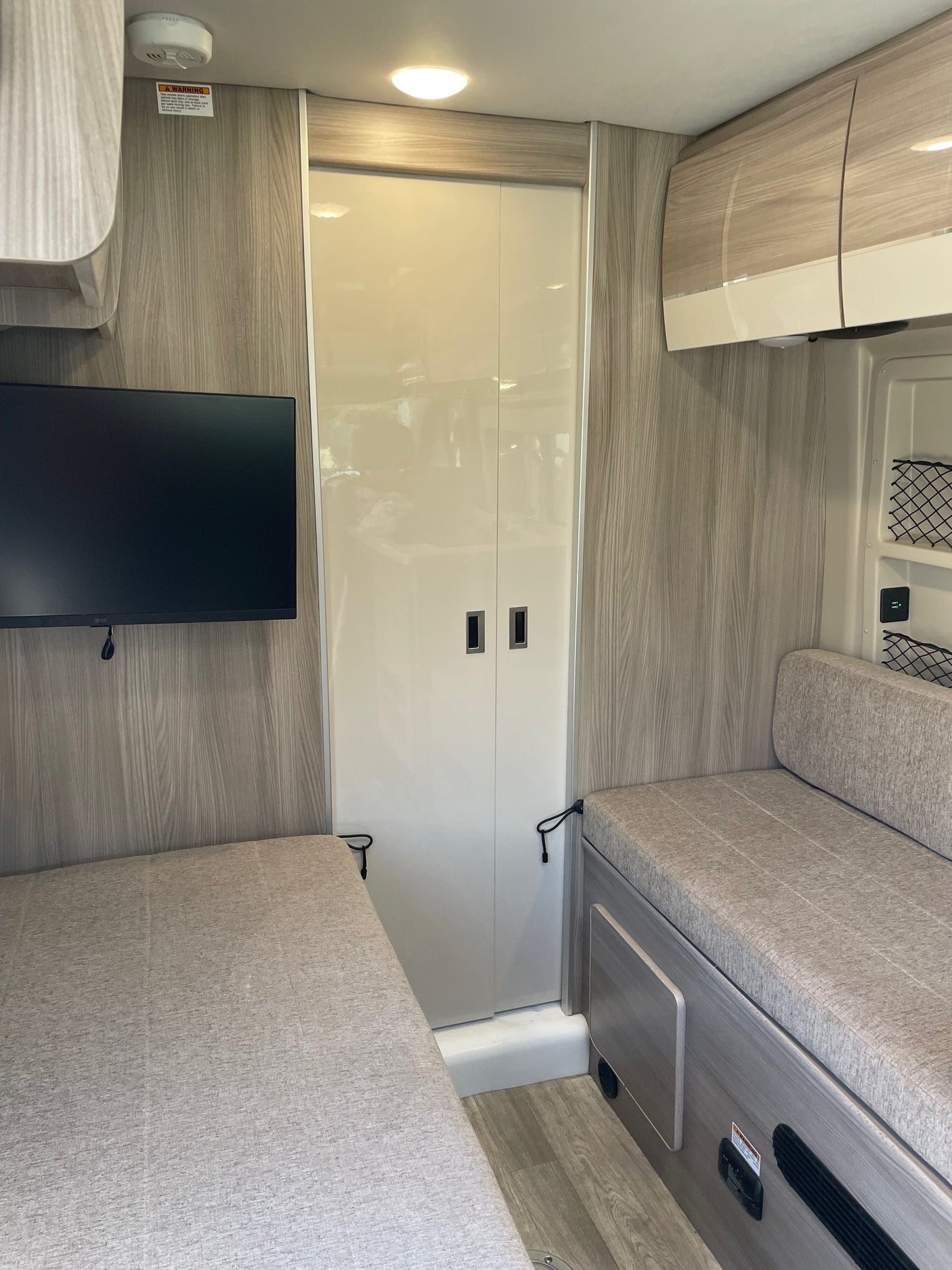 RV rental interior showcasing a modern, compact design. Features a bed, bench seating, TV, and an enclosed bathroom.