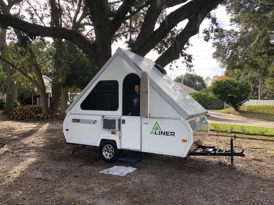 A person smiles from inside a white Aliner A-frame RV rental