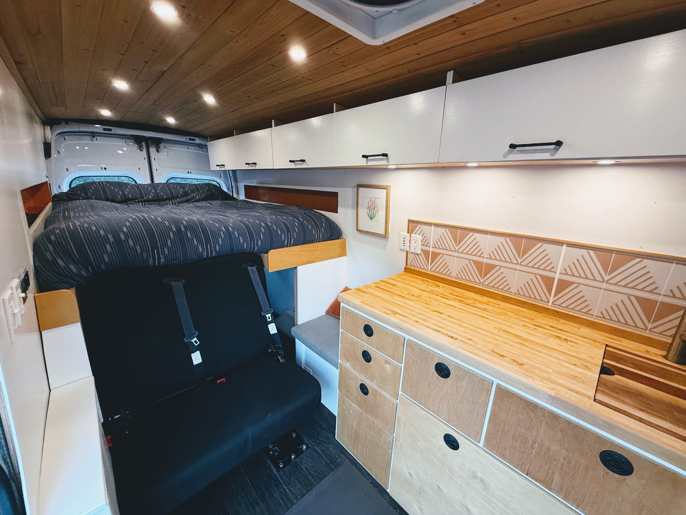 Cozy rv rental interior: wooden ceiling, built-in bed, bench seating, and a kitchenette with a tiled backsplash & wood counters.