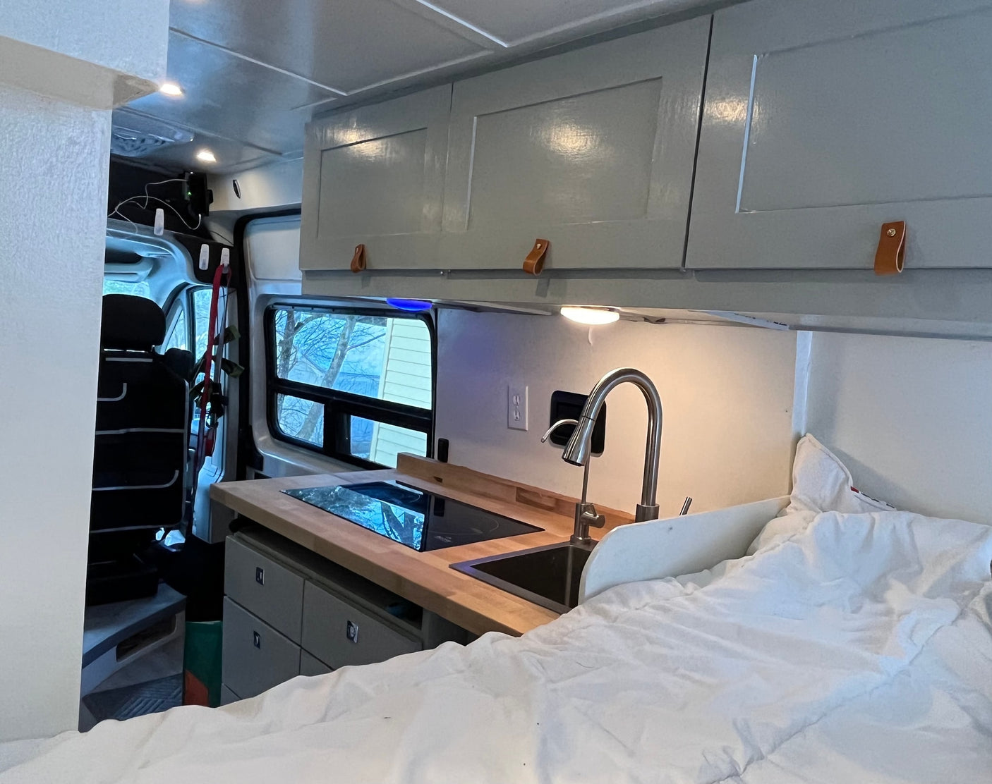 Inside an rv rental: functional kitchenette with cooktop & sink, comfy bed, and ample overhead cabinets.