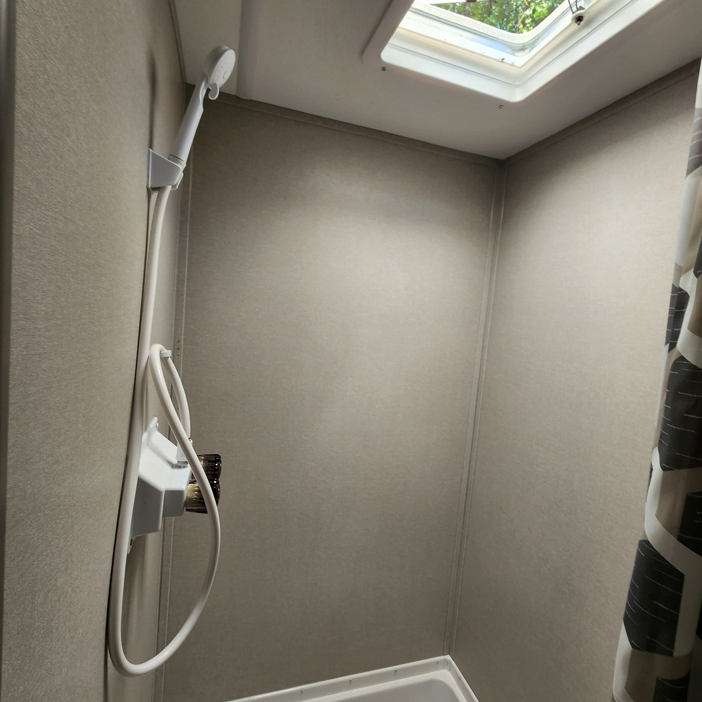Inside an RV rental shower: a compact space with a handheld shower, neutral walls, and a skylight for natural light.