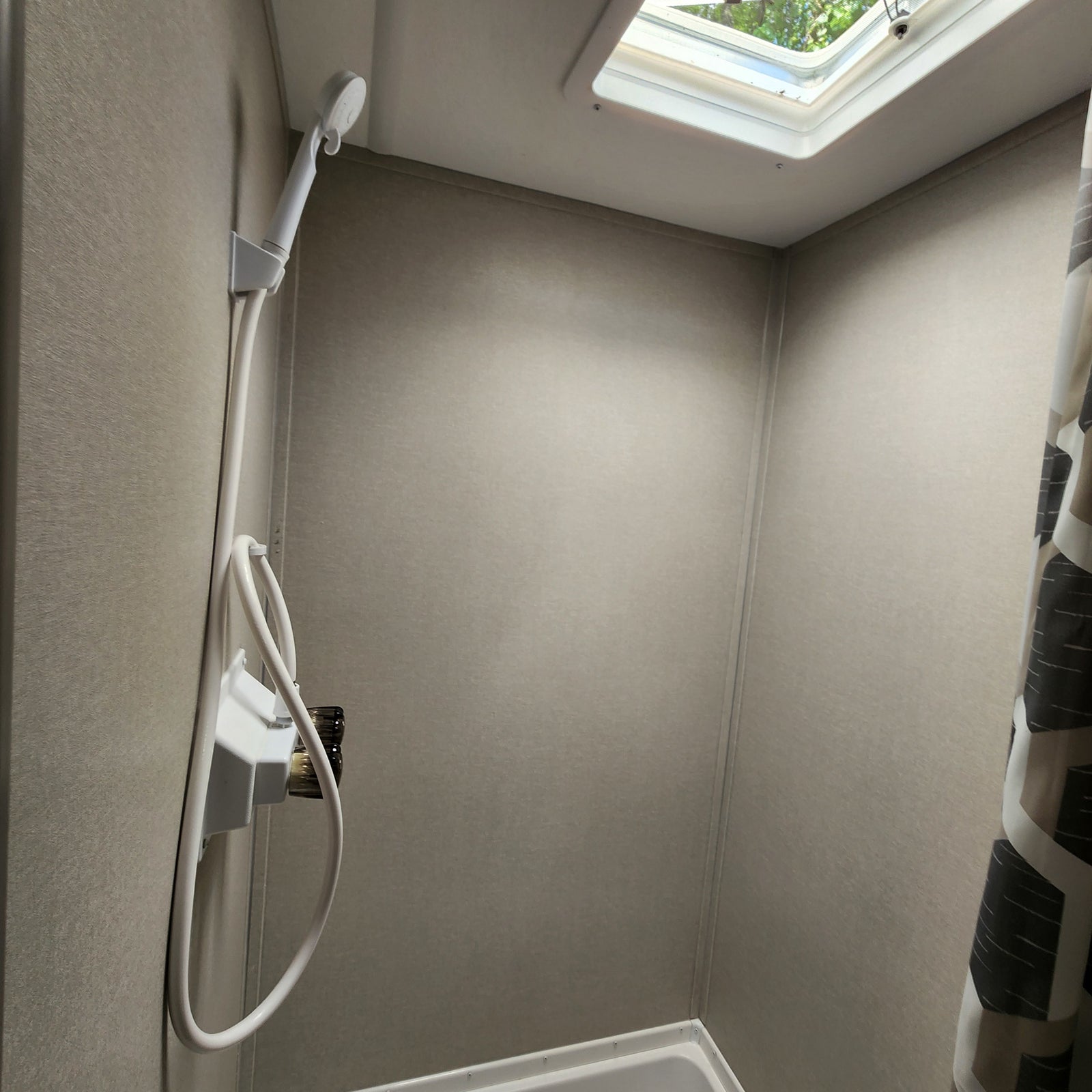 Inside an RV rental shower: a compact space with a handheld shower, neutral walls, and a skylight for natural light.