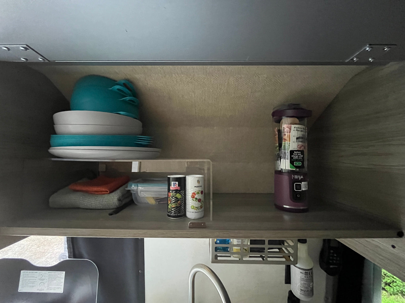 Organized RV rental kitchen cabinet with stacked dishes, spices, and a Ninja blender. Practical setup for compact spaces.