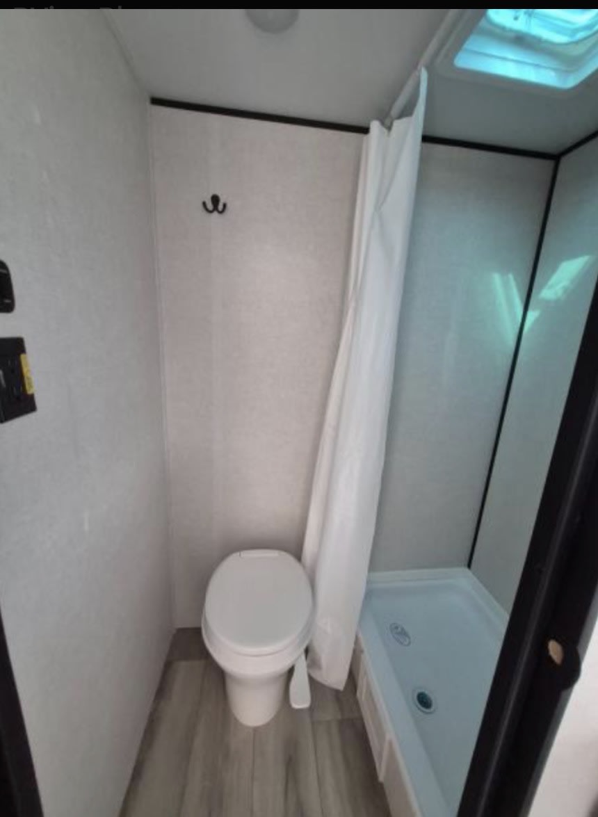Inside an RV rental, this compact bathroom features a toilet, shower, and ceiling skylight, ideal for travelers.