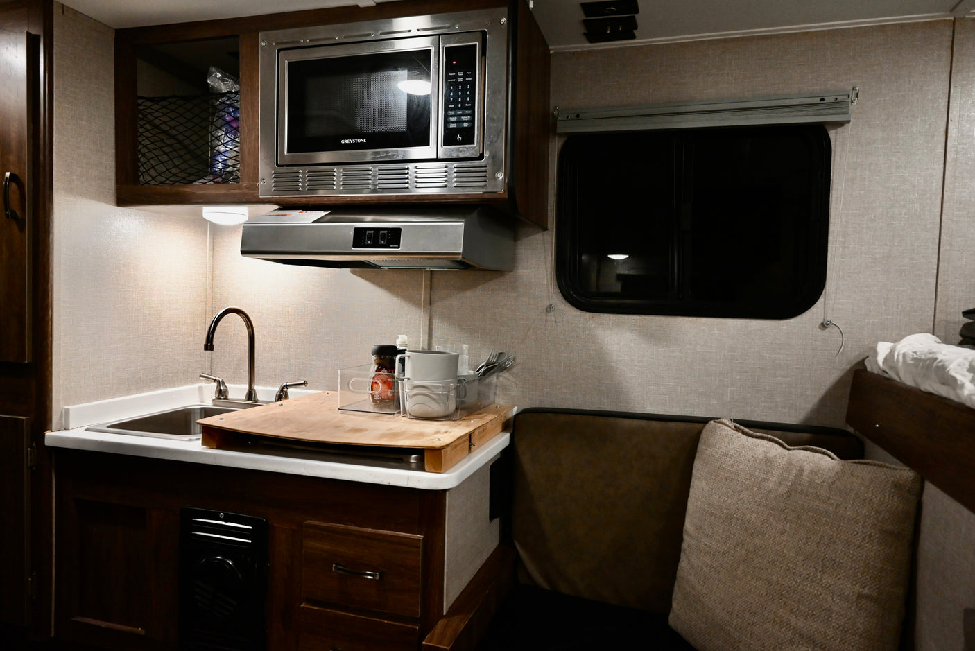 Compact RV rental kitchen features microwave, sink, and adjacent seating area with window, ideal for road trips.