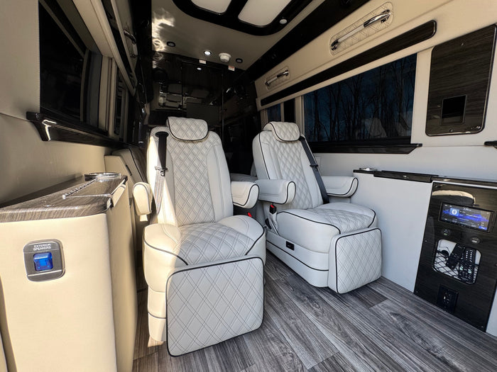 parked outdoors near a sand volleyball court with bare trees.|Explore with this dark gray Mercedes Sprinter RV rental. Parked on a sandy path near water