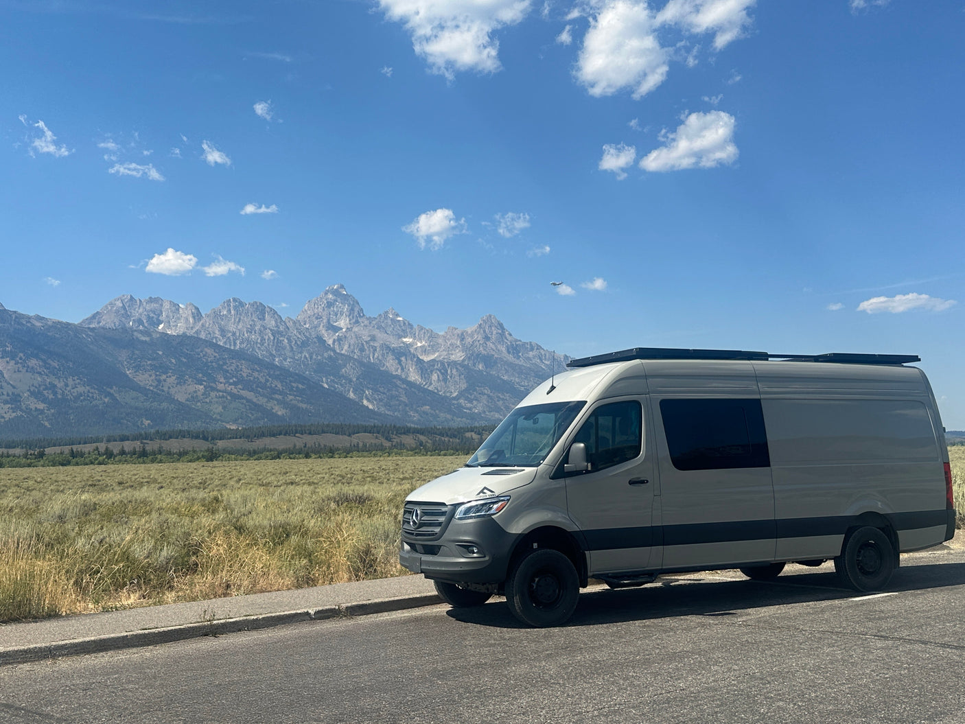 Grey Mercedes Sprinter RV rental van overlooks Grand Teton mountains on a sunny day. Adventure awaits!