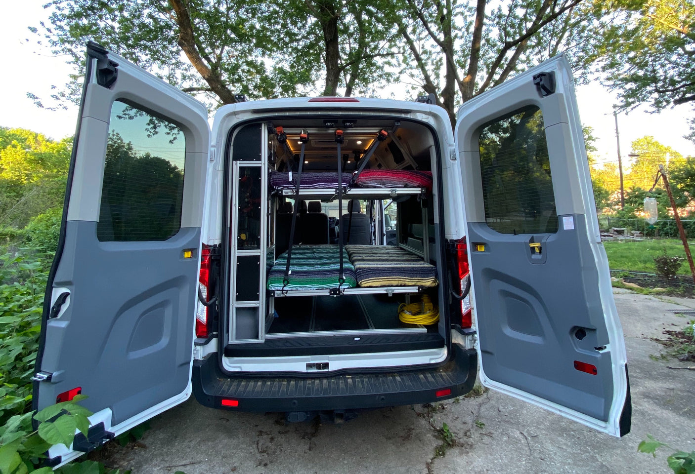 Inside this RV rental, open rear doors reveal two bunk beds with colorful blankets, ideal for travel.