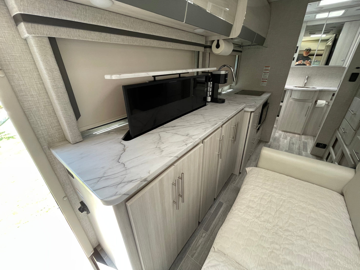 RV rental's modern kitchen: sleek marble-look counters, pop-up TV, light wood cabinets, and compact amenities.