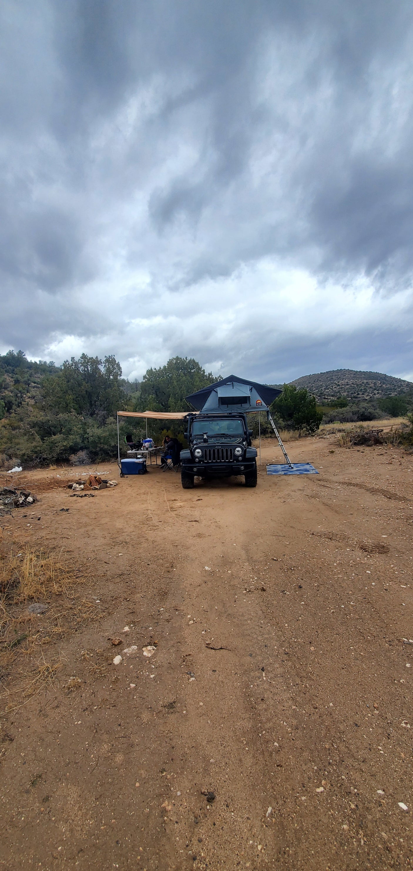 An overlanding Jeep with rooftop tent & awning setup at a dirt campsite. A robust RV rental alternative for outdoor adventure.