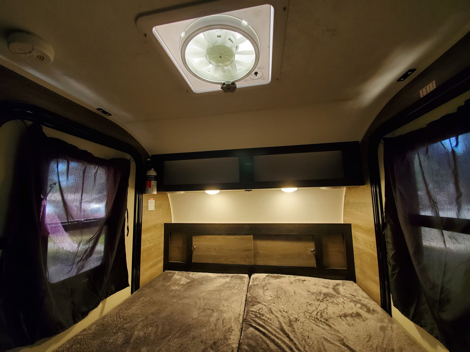 Inside an RV rental: a comfortable bed with overhead lights, fan, and storage. Ideal for road trips.
