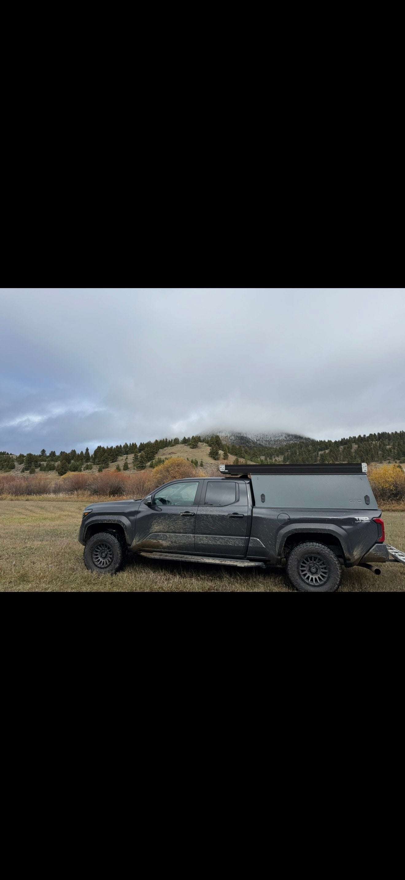 Rugged dark truck with pop-top camper in a cloudy mountain landscape. An ideal off-road adventure rv rental option.