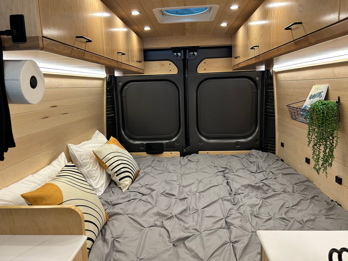 Cozy RV rental bedroom with wood paneling, overhead cabinets, and a comfy bed. Perfect for van life adventures!