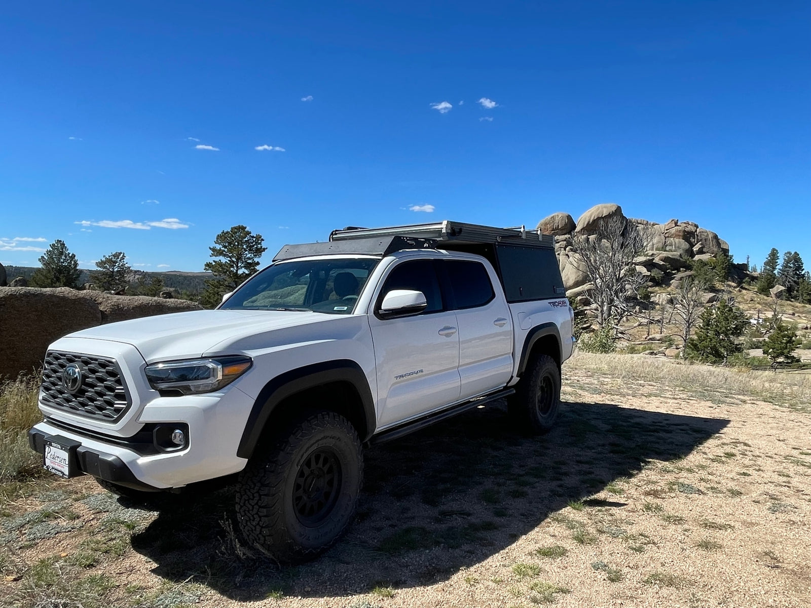 White Toyota Tacoma truck with an overland camper setup, parked off-road in a scenic, rocky area. An adventurous alternative to standard rv rental.