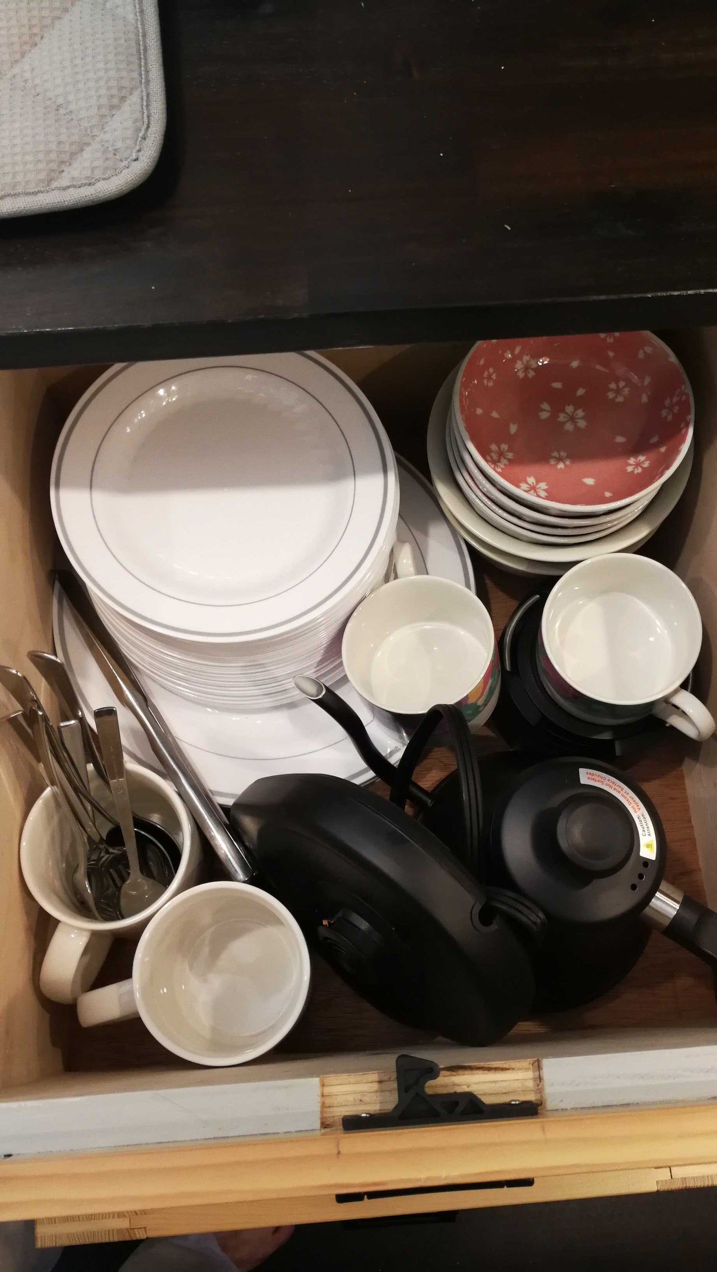 RV rental kitchen essentials: stacked white plates, patterned bowls, mugs, and a black electric kettle organized in a drawer.
