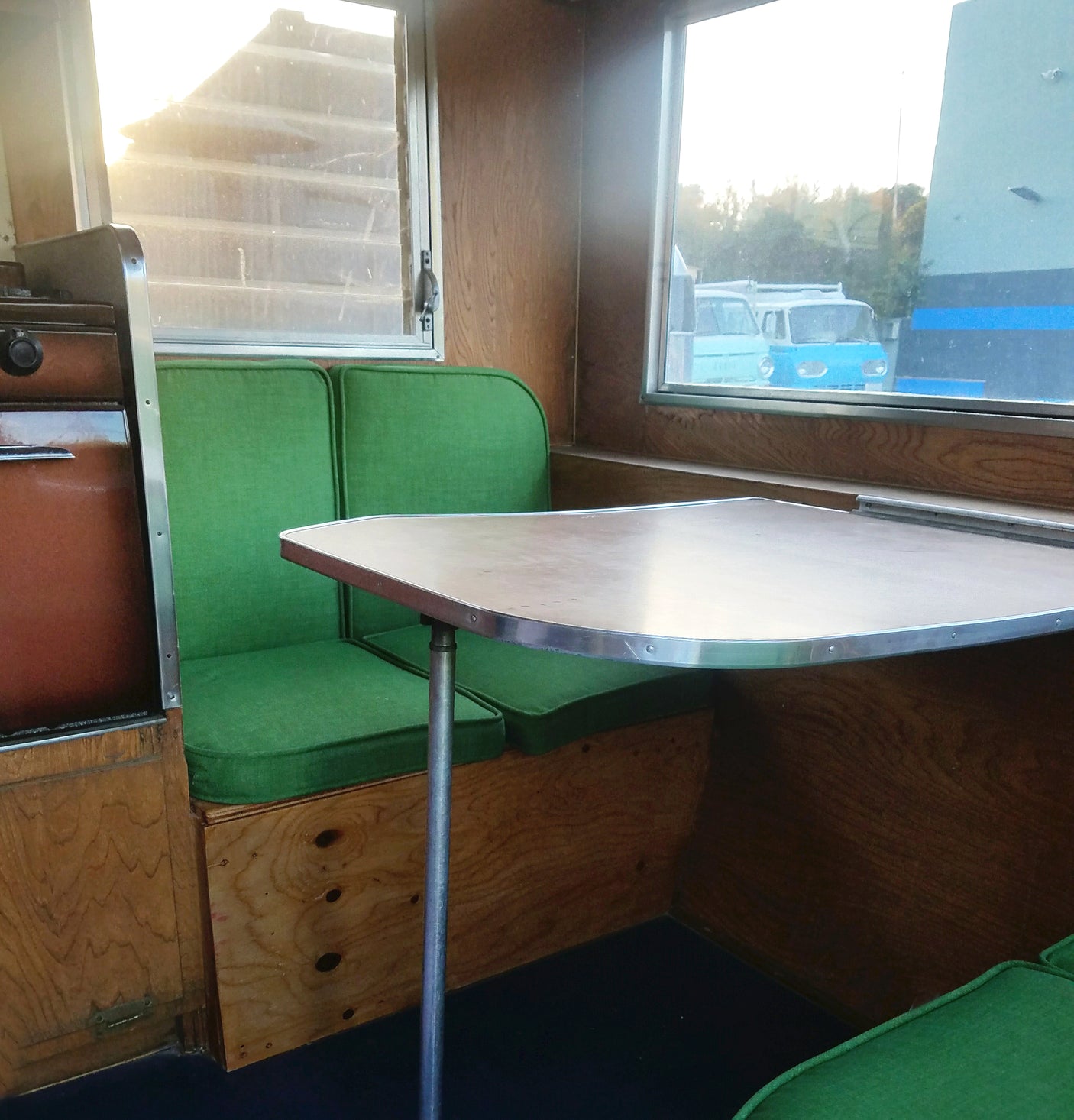 This RV rental interior features a wooden dining area with bright green cushions, and a large window view.