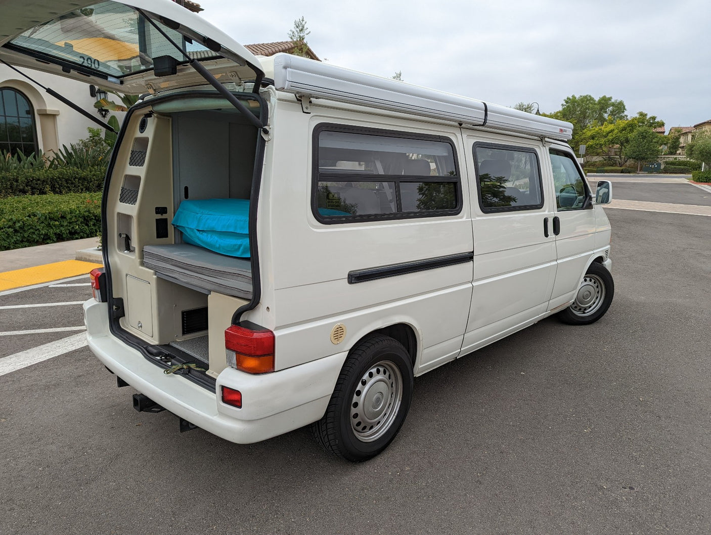 White camper van, perfect for RV rental adventures, with open rear hatch showing sleeping setup.
