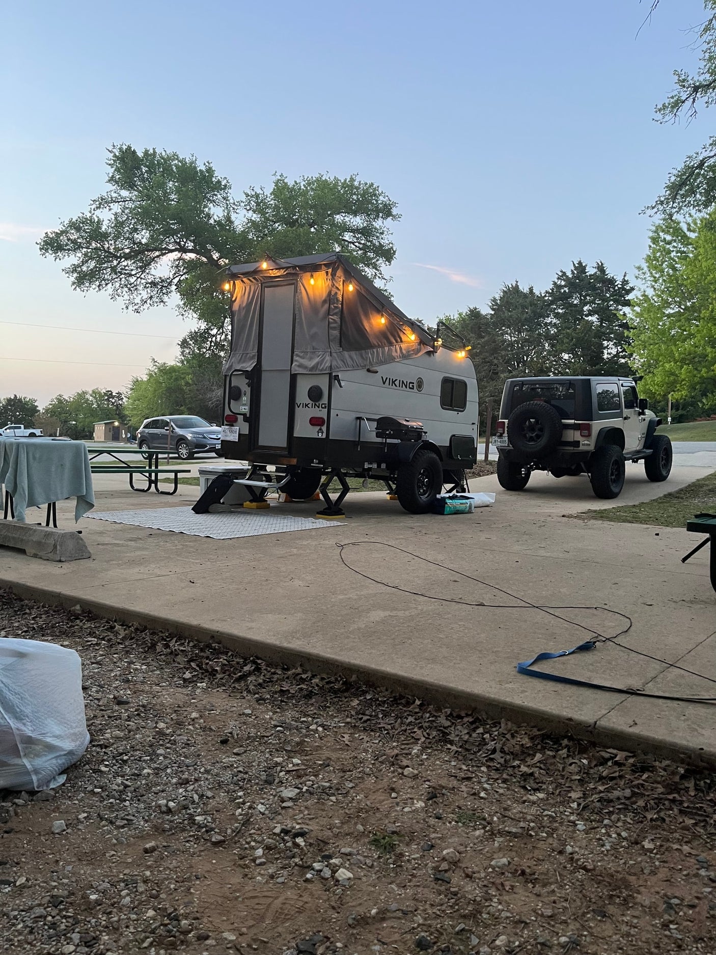 RV rental: A Viking pop-up camper with string lights is set up at a campsite next to a Jeep Wrangler at dusk.