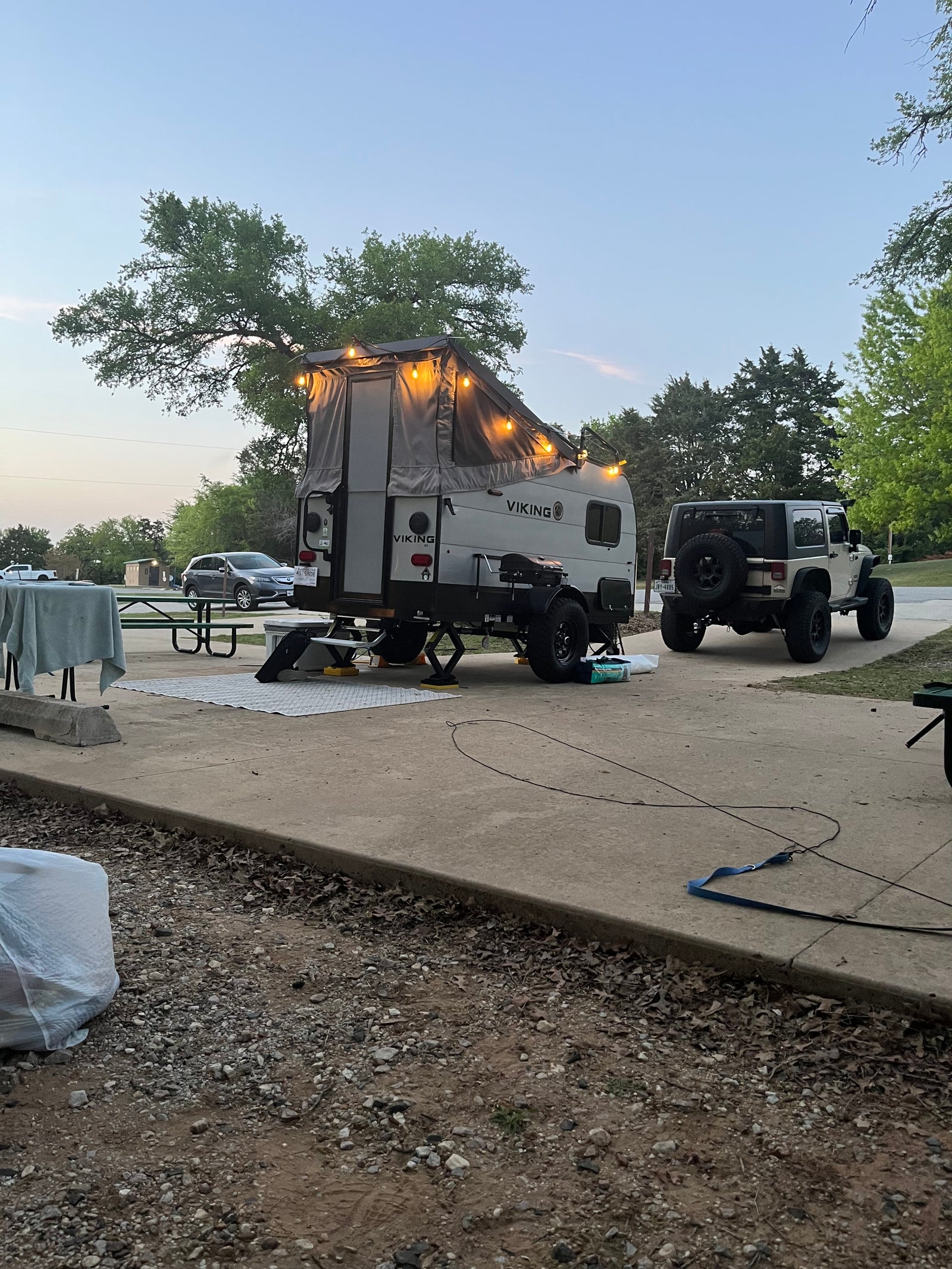 RV rental: A Viking pop-up camper with string lights is set up at a campsite next to a Jeep Wrangler at dusk.
