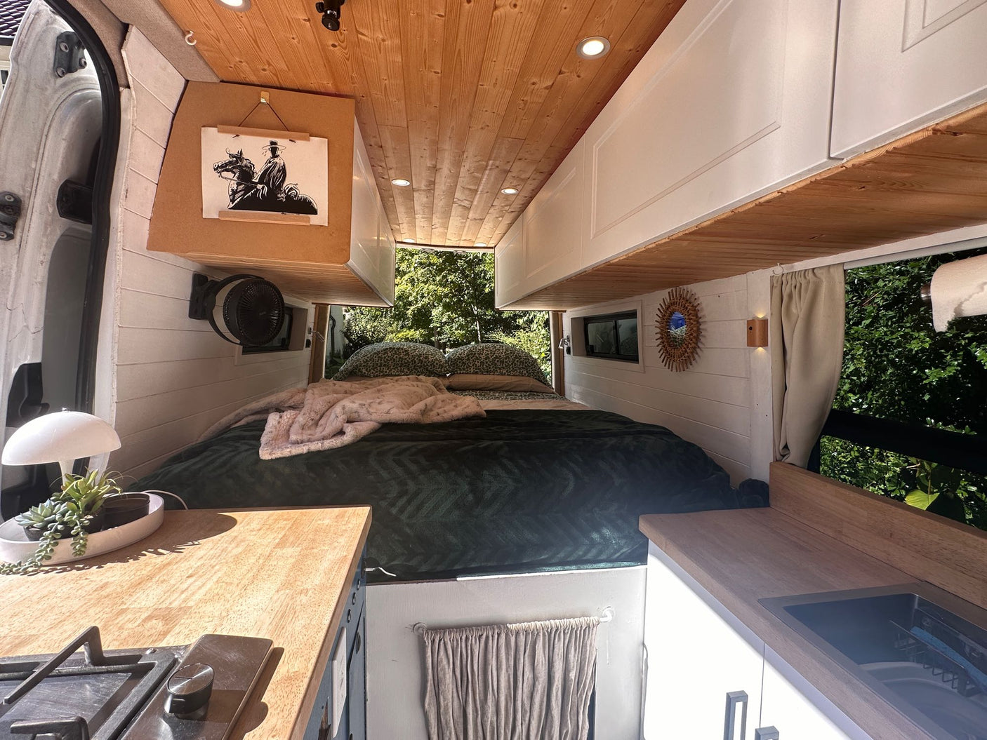 is parked with its door open in a scenic forest setting.|Cozy white camper van (rv rental) parked under a starry blue night sky. Warm light glows from its window