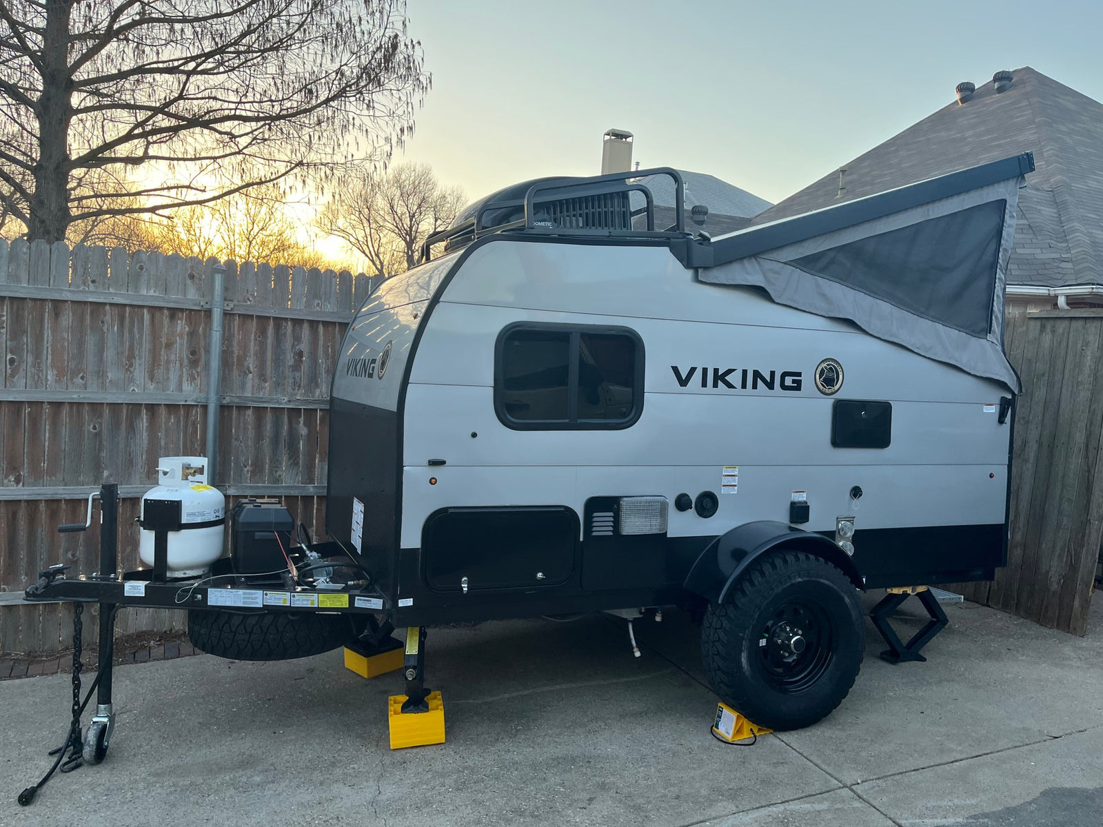 A gray and black Viking pop-up travel trailer, well-equipped for rv rental, parked on concrete with stabilizing jacks.
