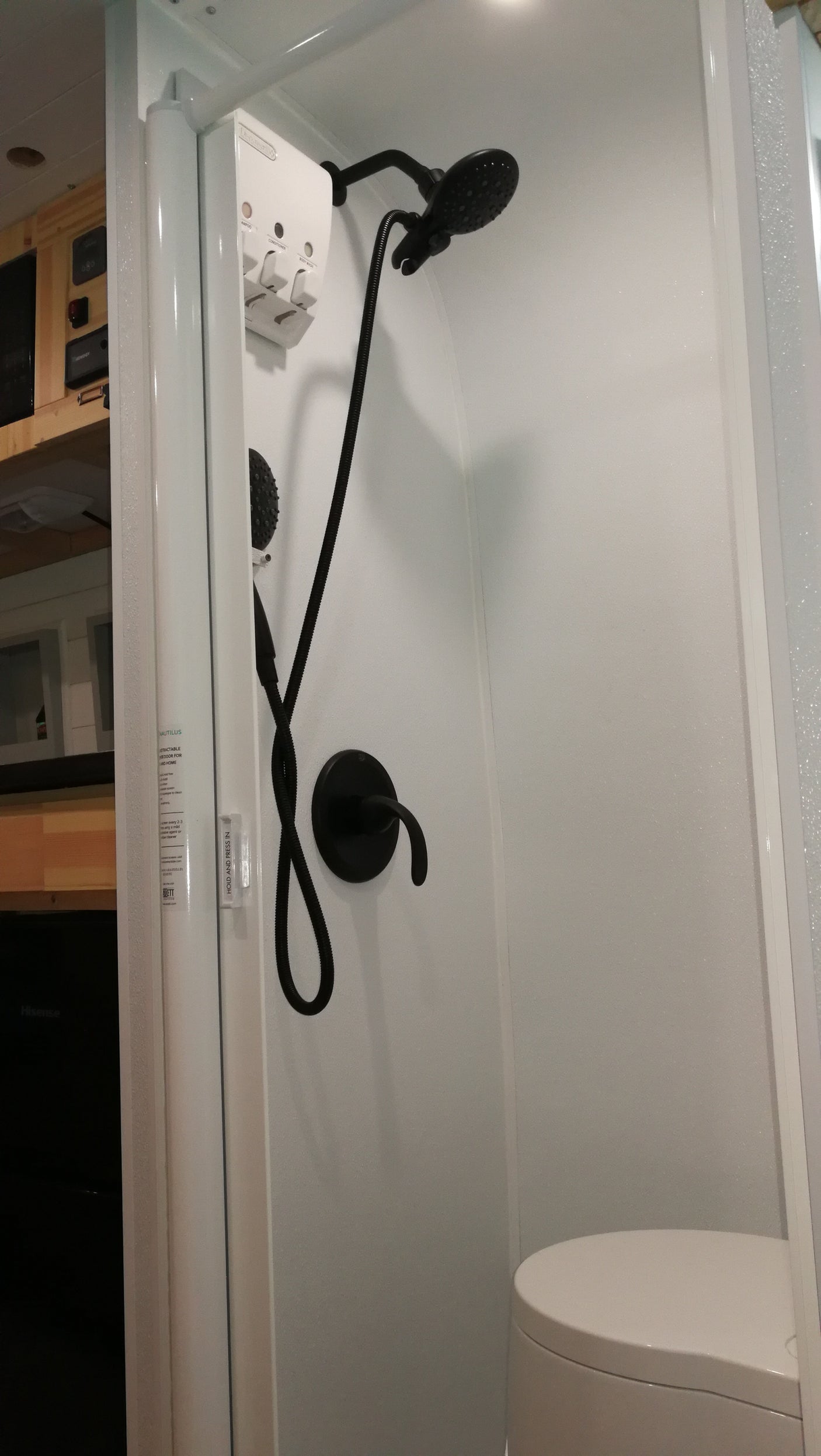 Modern RV rental bathroom: white shower stall with sleek black fixtures, wall dispenser, and compact toilet. Ideal for road trips.