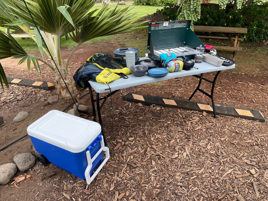 RV rental trip essentials: Coleman stove, cooking gear, cooler on a table, ready for campsite dining.