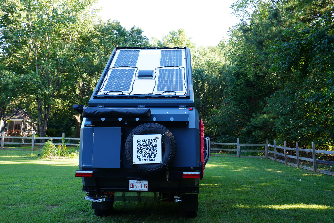 This rv rental trailer features rooftop solar panels & a "RENT ME!" QR code on its spare tire. Ideal for off-grid adventures!