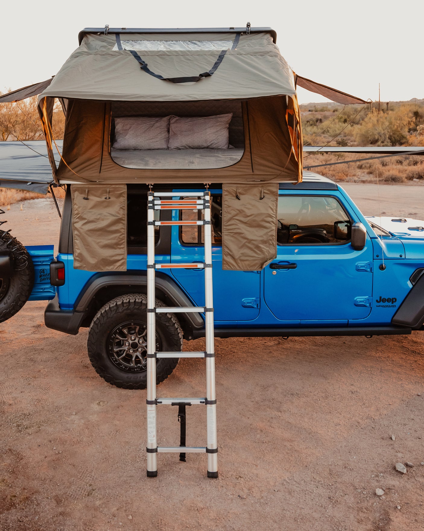 Blue Jeep Wrangler with a deployed rooftop tent and ladder for an overland rv rental adventure.