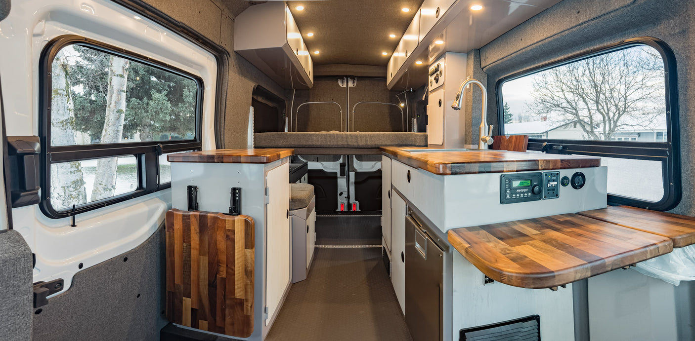 Inside a well-appointed RV rental, showcasing a compact kitchen with a sink, wooden counters, and comfortable rear bed.